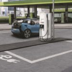 Blå elbil laddas vid en vit laddstation på en parkeringsplats.