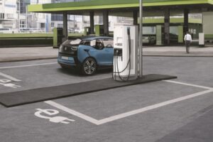 Blå elbil laddas vid en vit laddstation på en parkeringsplats.