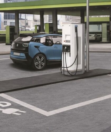 Blå elbil laddas vid en vit laddstation på en parkeringsplats.