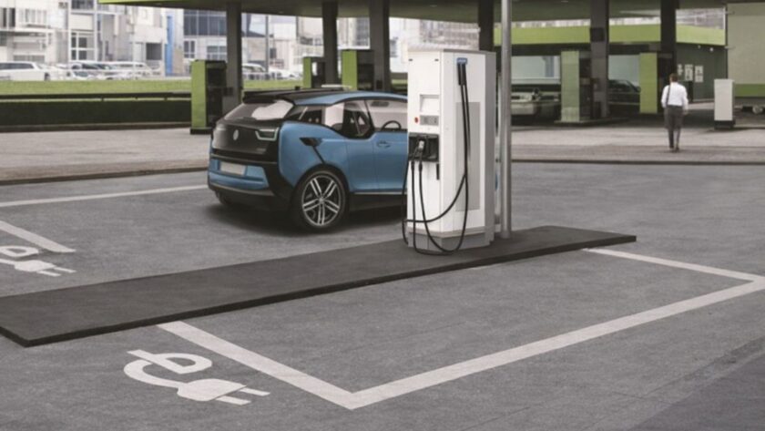 Blå elbil laddas vid en vit laddstation på en parkeringsplats.