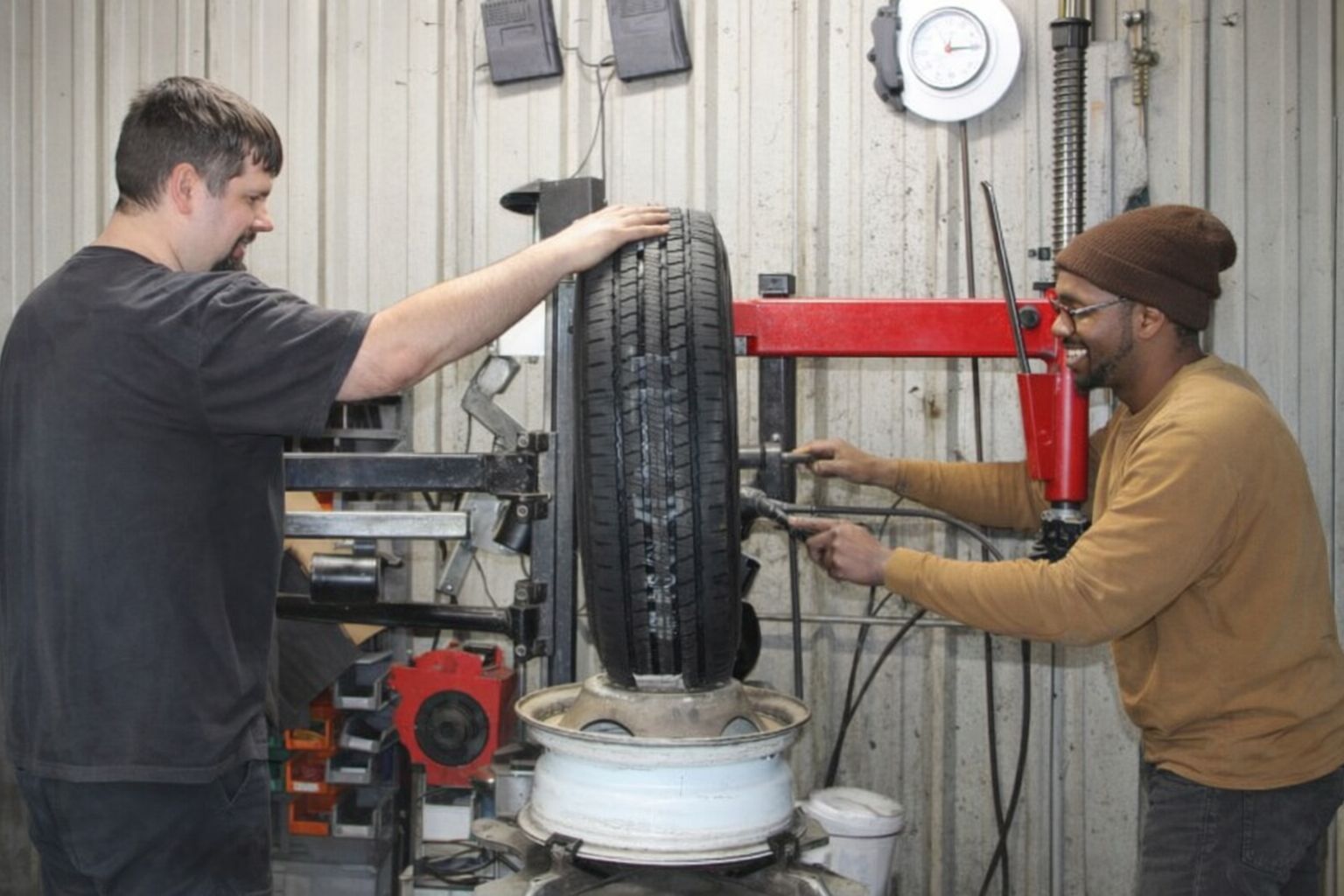 Två män balanserar ett däck i en verkstad, relevant för däckverkstadsartikeln.