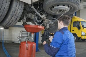 Mekaniker i blå arbetskläder utför underhåll på undersidan av en lastbil.