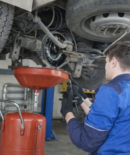 Mekaniker i blå arbetskläder utför underhåll på undersidan av en lastbil.